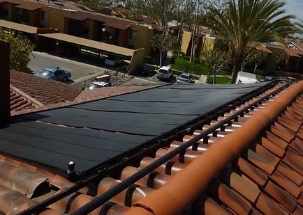 Solar panel installer working on rooftop under a clear blue sky. He wears a white helmet, orange jacket, and gloves.