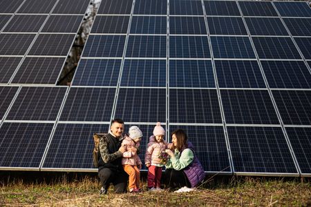 Two people give thumbs up next to a solar panel inverter on a wall.