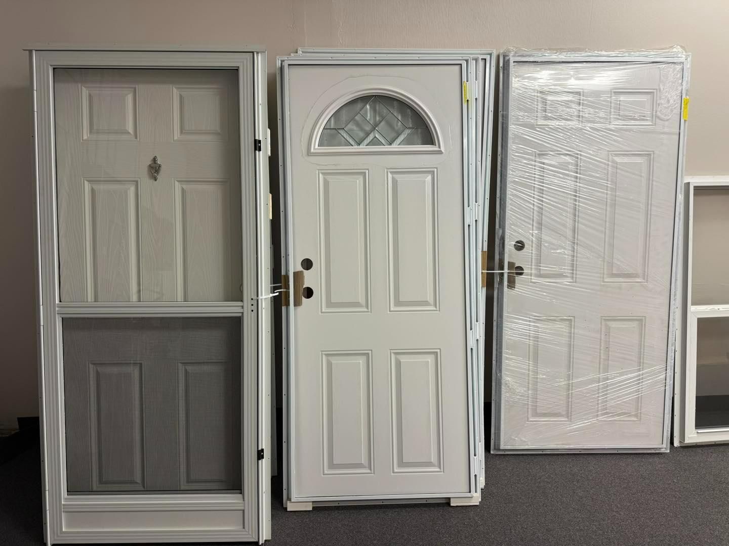 Three white exterior doors of different styles standing on a black carpet.