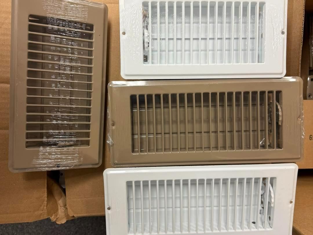 Four rectangular HVAC vent covers, two white, one tan, one wrapped in plastic.