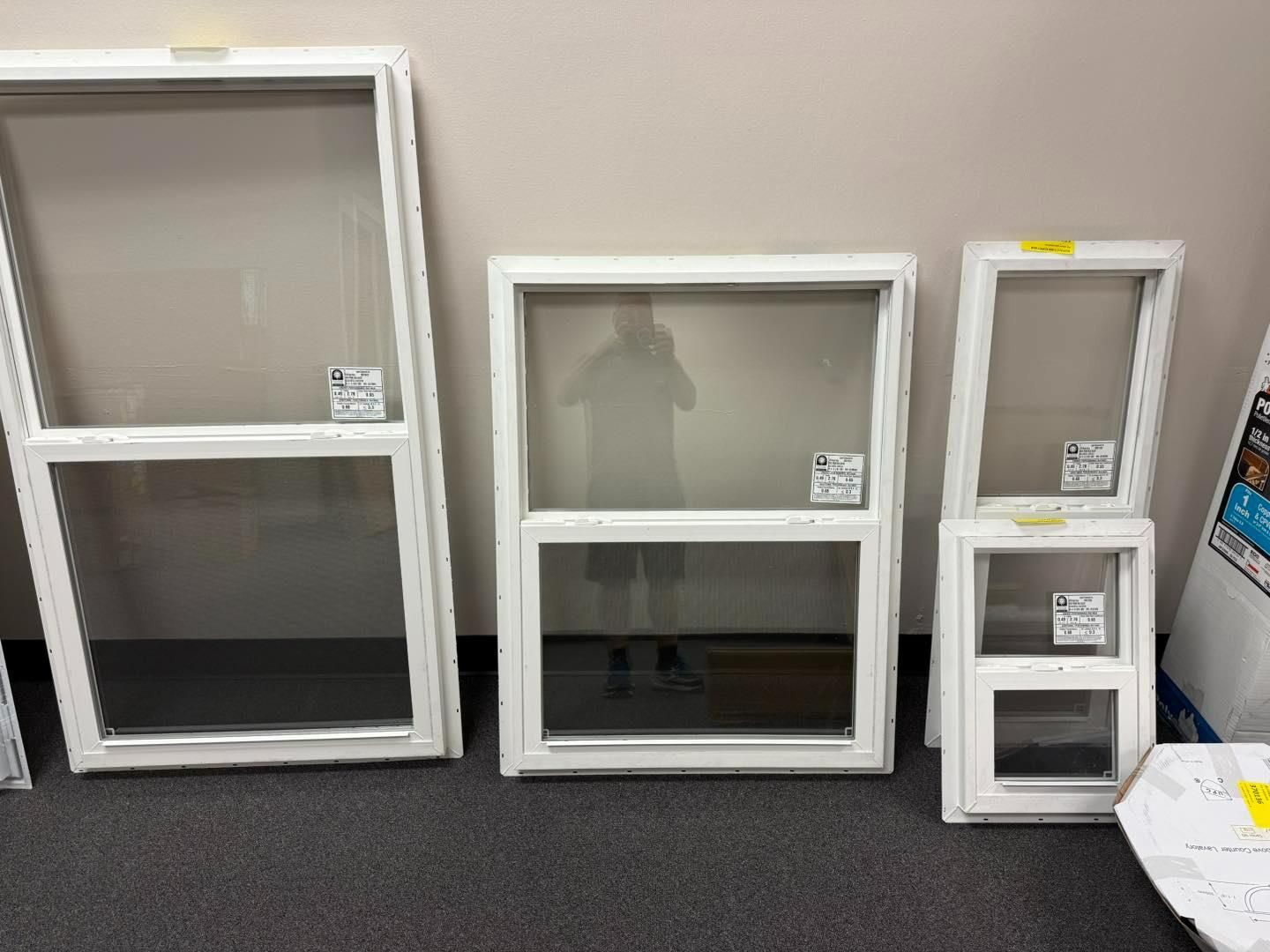 Three white framed windows of varying sizes leaning against a wall.