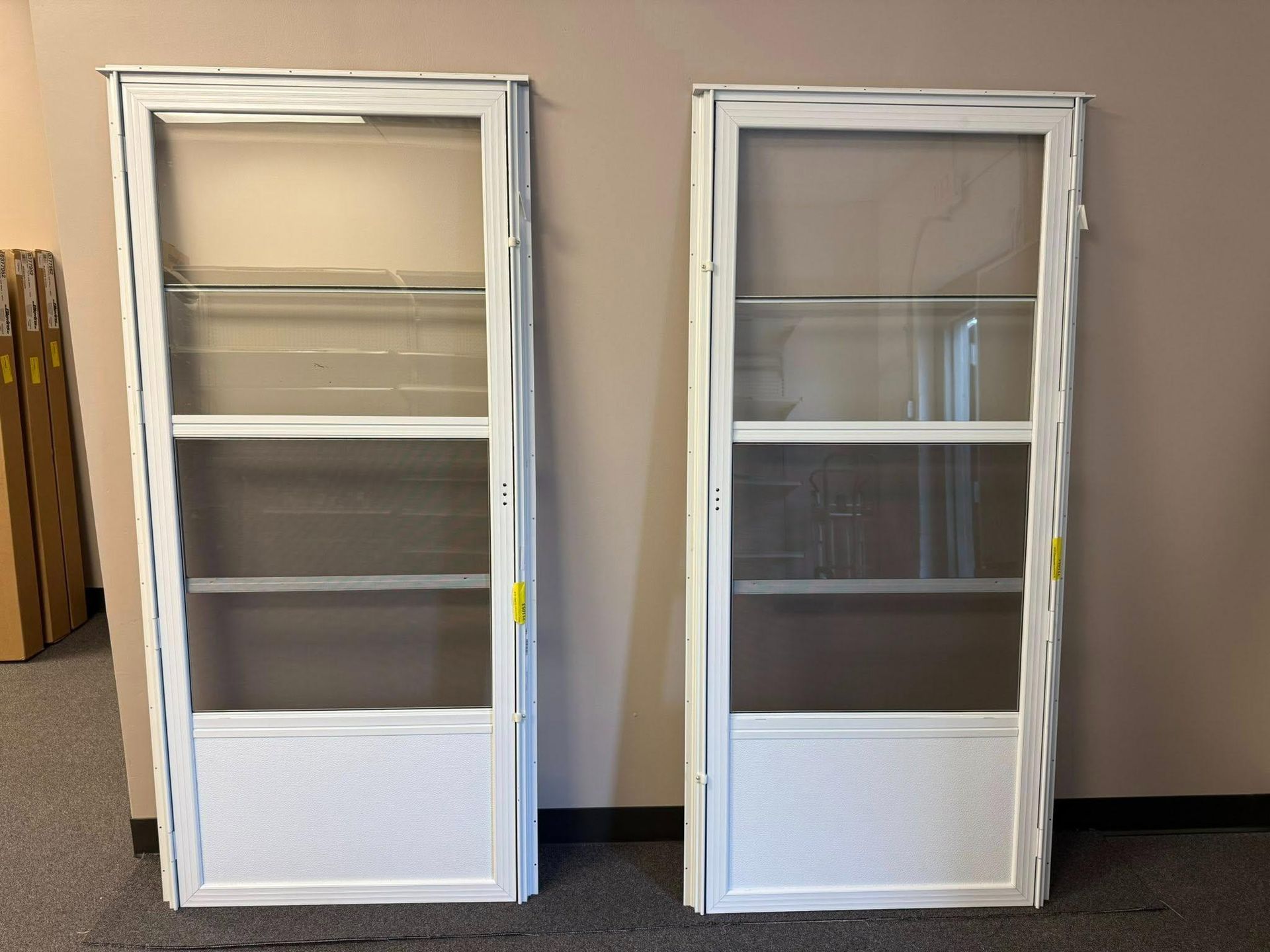Two white screen doors with glass and mesh panels, standing upright against a neutral wall.