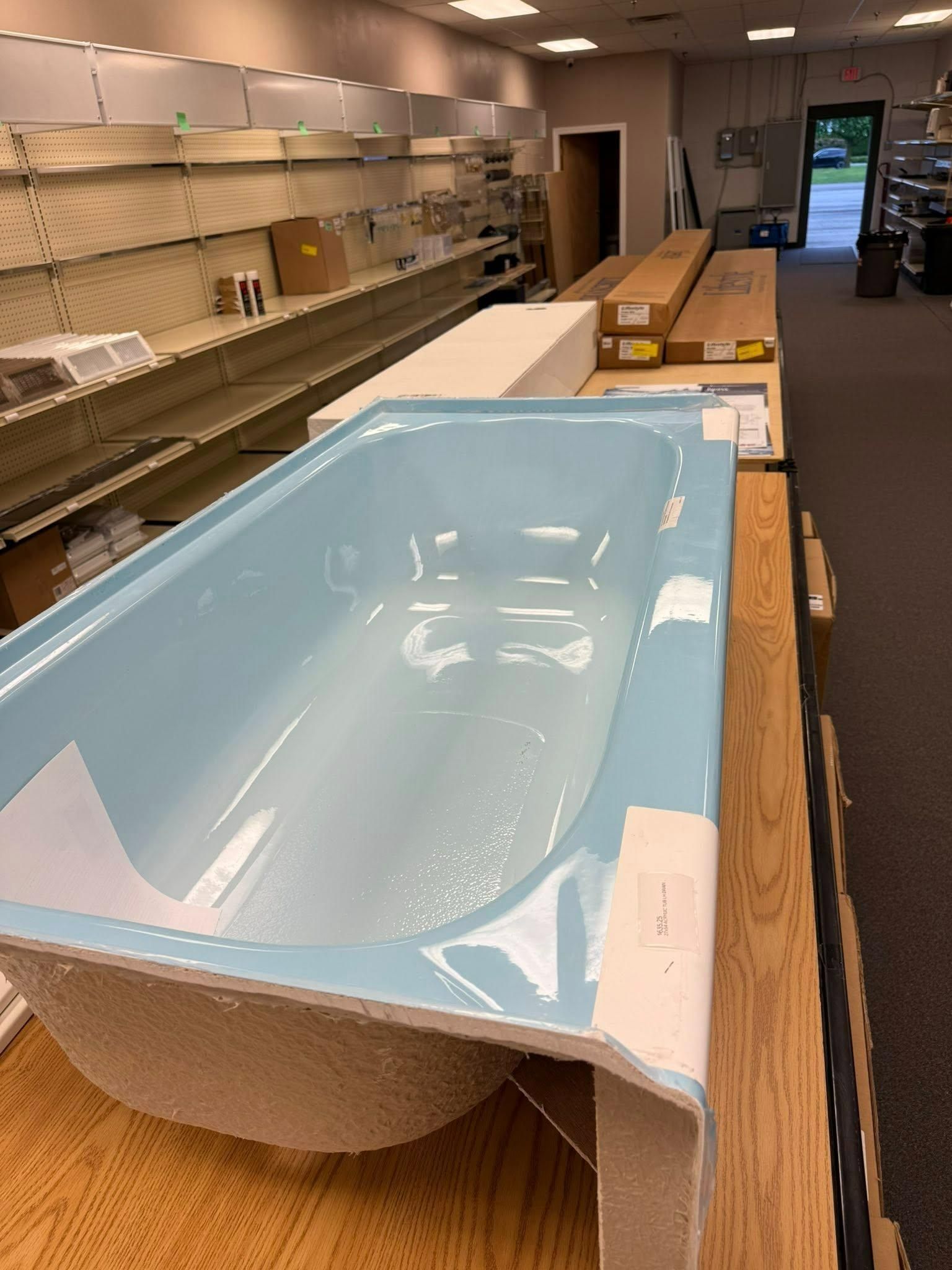 Light blue bathtub on display in a store, with empty shelves in the background.