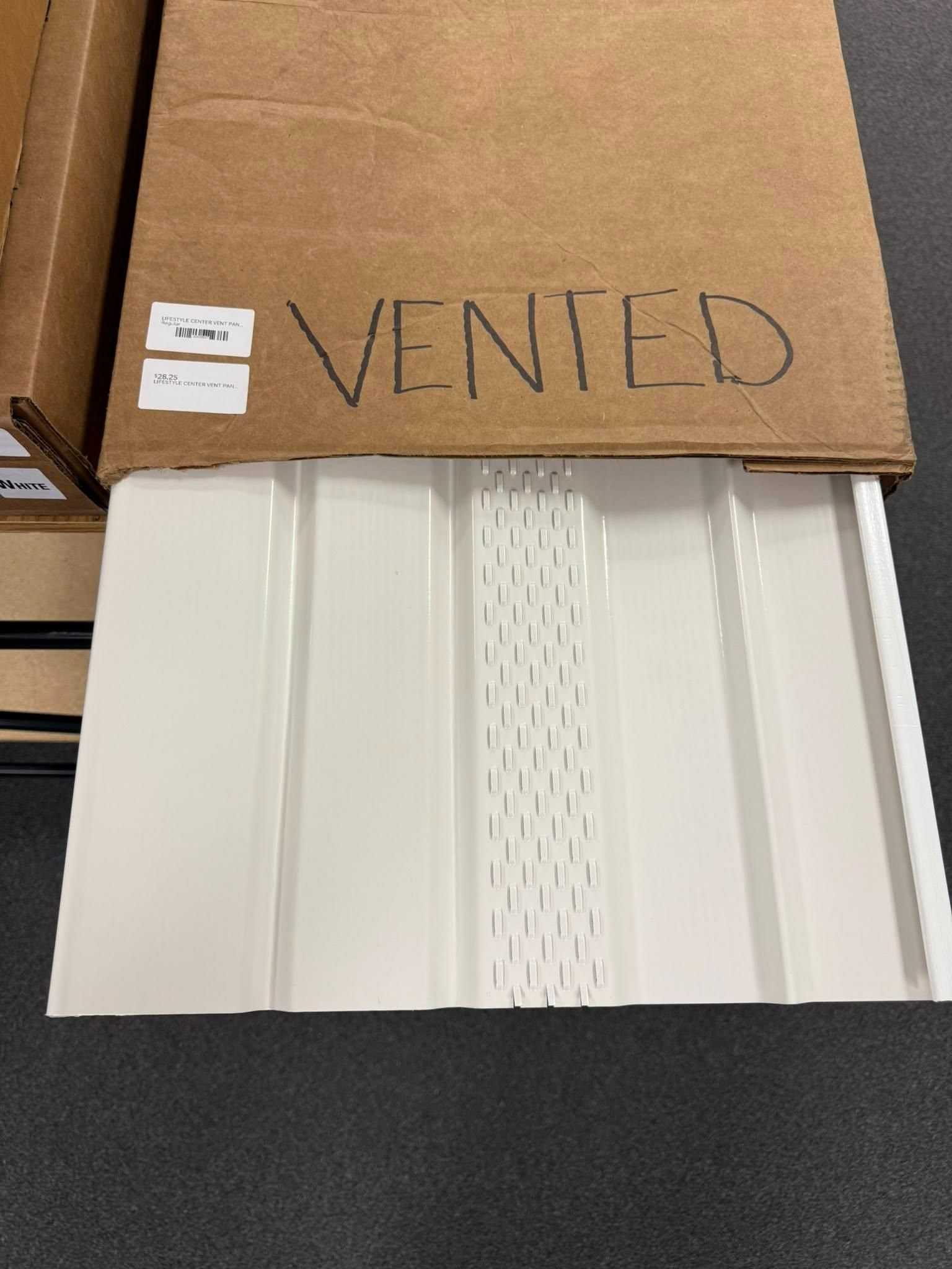 White, vented siding panel partially out of a cardboard box. 