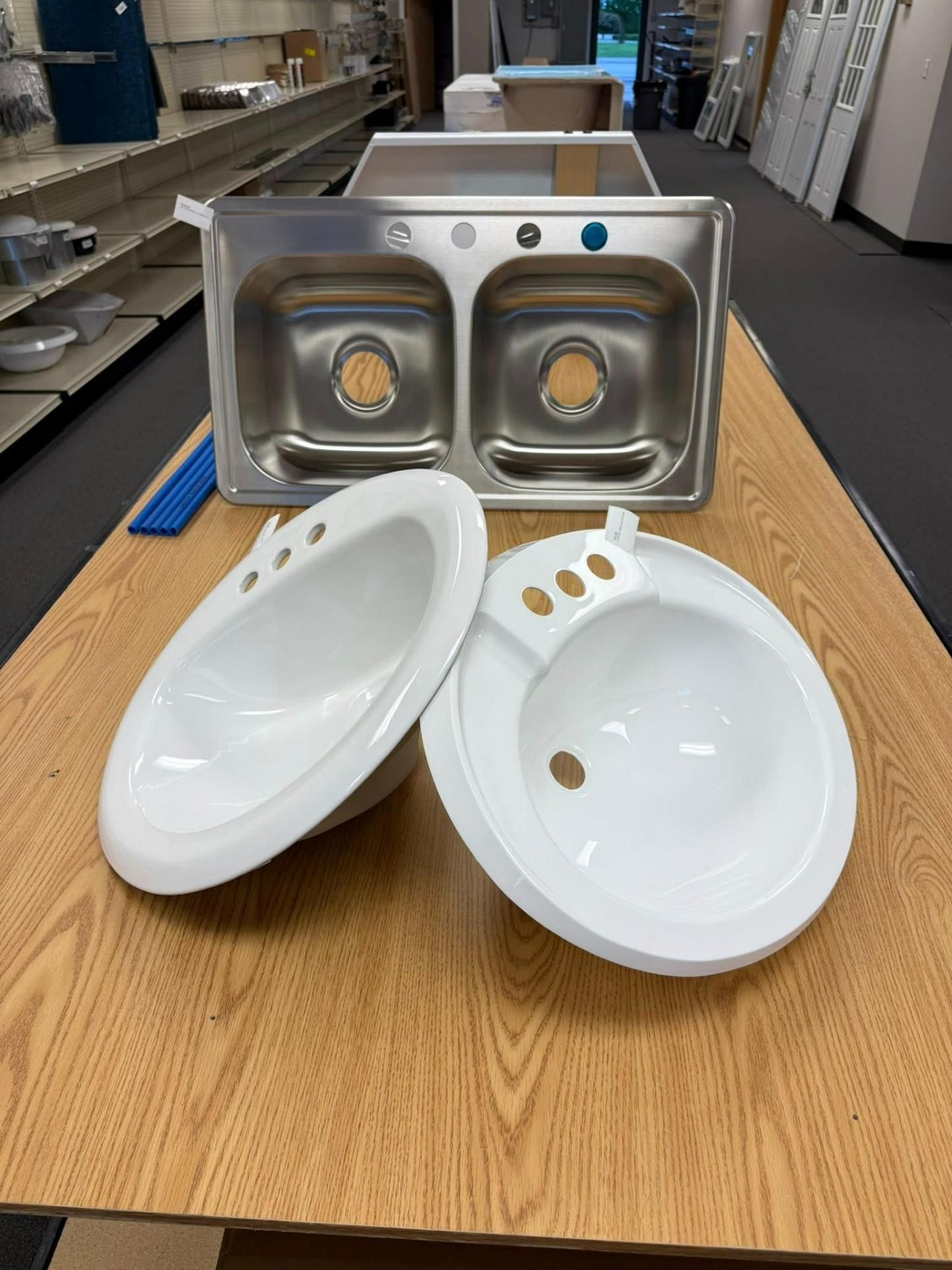 Stainless steel kitchen sink and two white bathroom sinks on a wooden table.