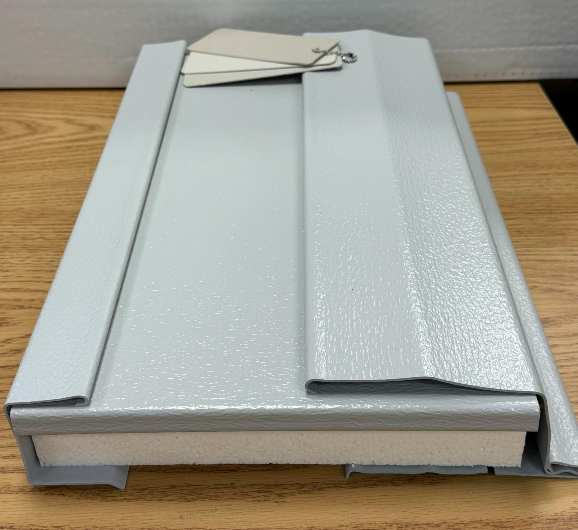 Light gray metal sample with attached paint color swatches on a wood surface.