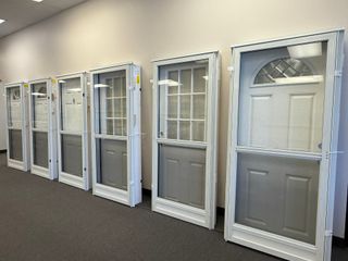 Row of white screen doors on display in a showroom. Each has a different style and glass design.