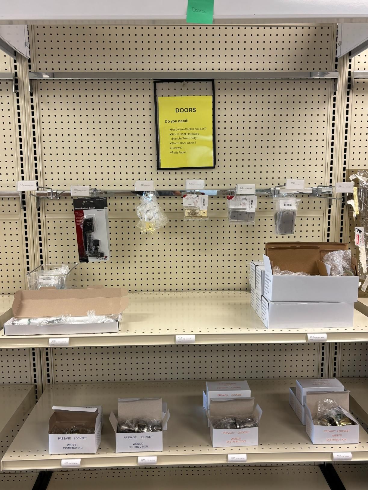 Empty store shelf with a few hardware items and a yellow sign.