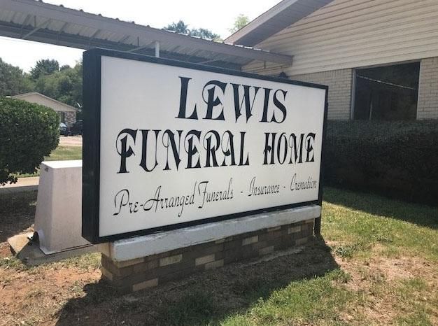 Lewis Funeral Home sign in white and black outside a brick building.