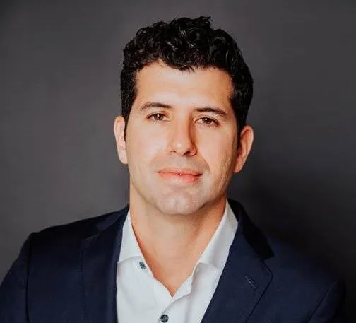 Studio portrait of a man in a dark blazer and light shirt against a gray background