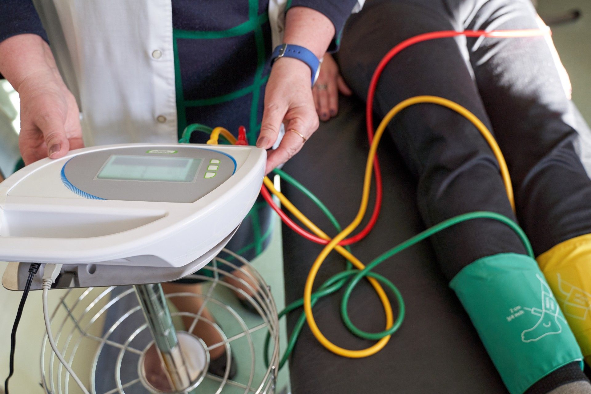 Doctor using blood pressure monitor on a patient’s arm with colored cuffs and wires