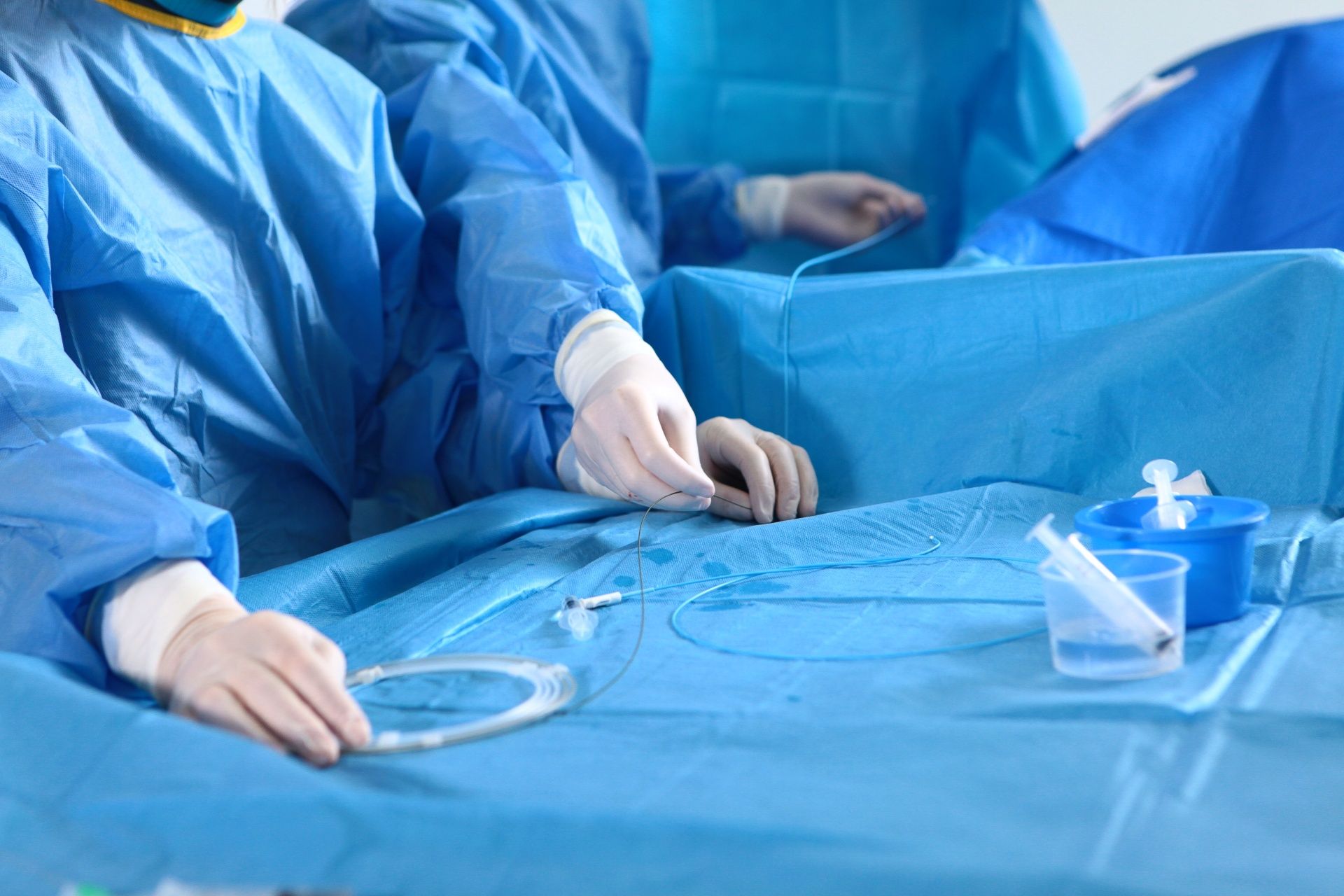 Surgeons in blue gowns and gloves working with medical instruments on a sterile operating table