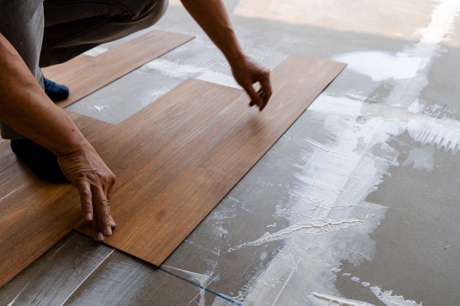 Person installing wood flooring planks on a concrete floor with adhesive.