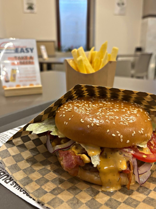 Cheeseburger con pancetta e formaggio fuso su carta a quadretti, con patatine fritte sullo sfondo.