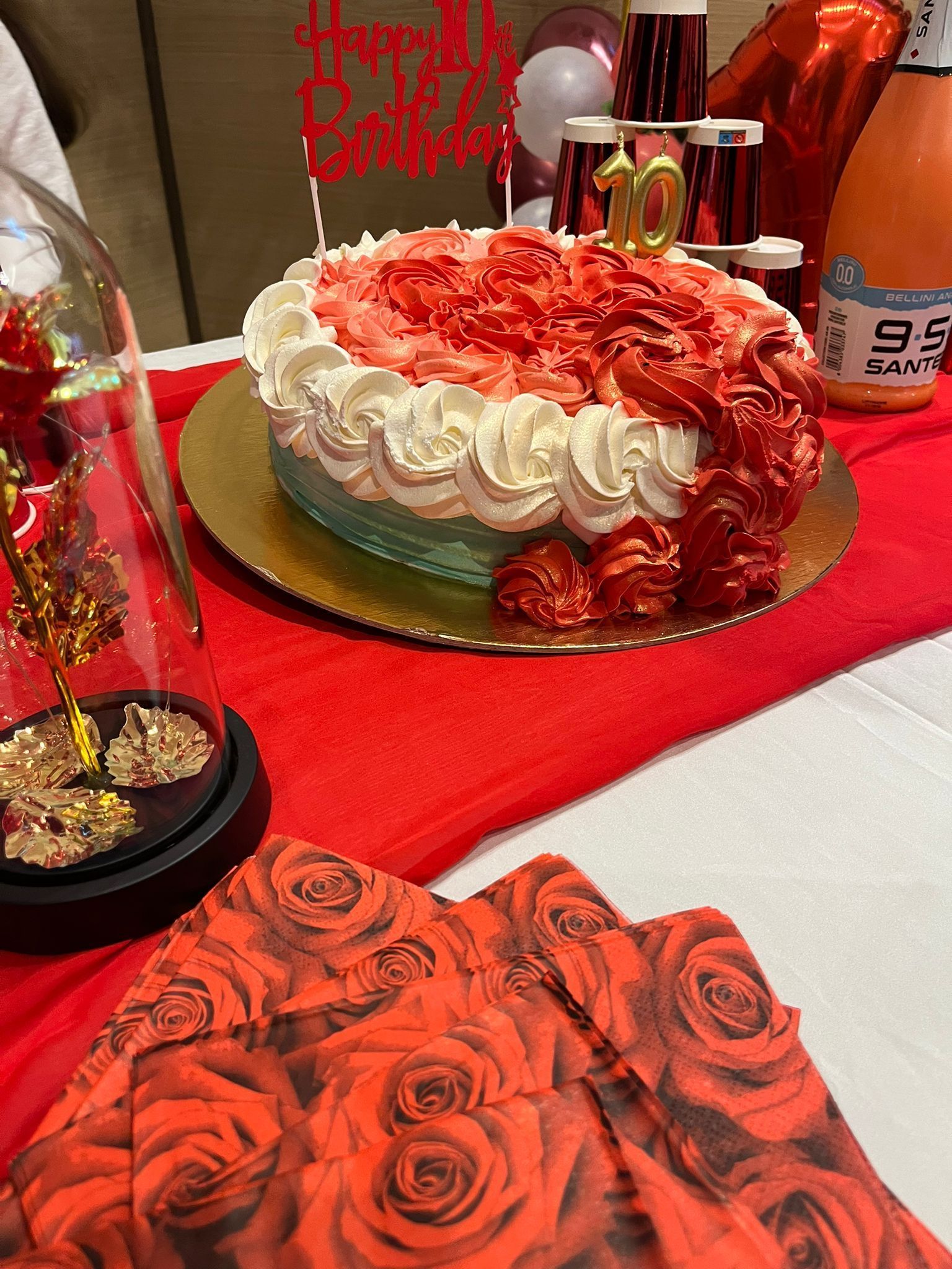 Torta di rose rosse e bianche con regali e decorazioni abbinati su una tovaglia rossa.