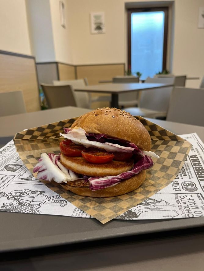 Un hamburger su un tavolo in una mensa, con cipolla rossa, pomodoro e un vassoio rivestito di carta a quadretti.