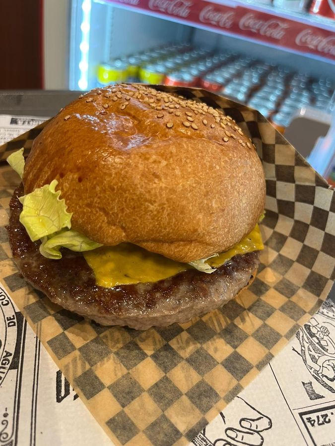 Cheeseburger con panino al sesamo, lattuga e formaggio fuso su carta a quadretti.