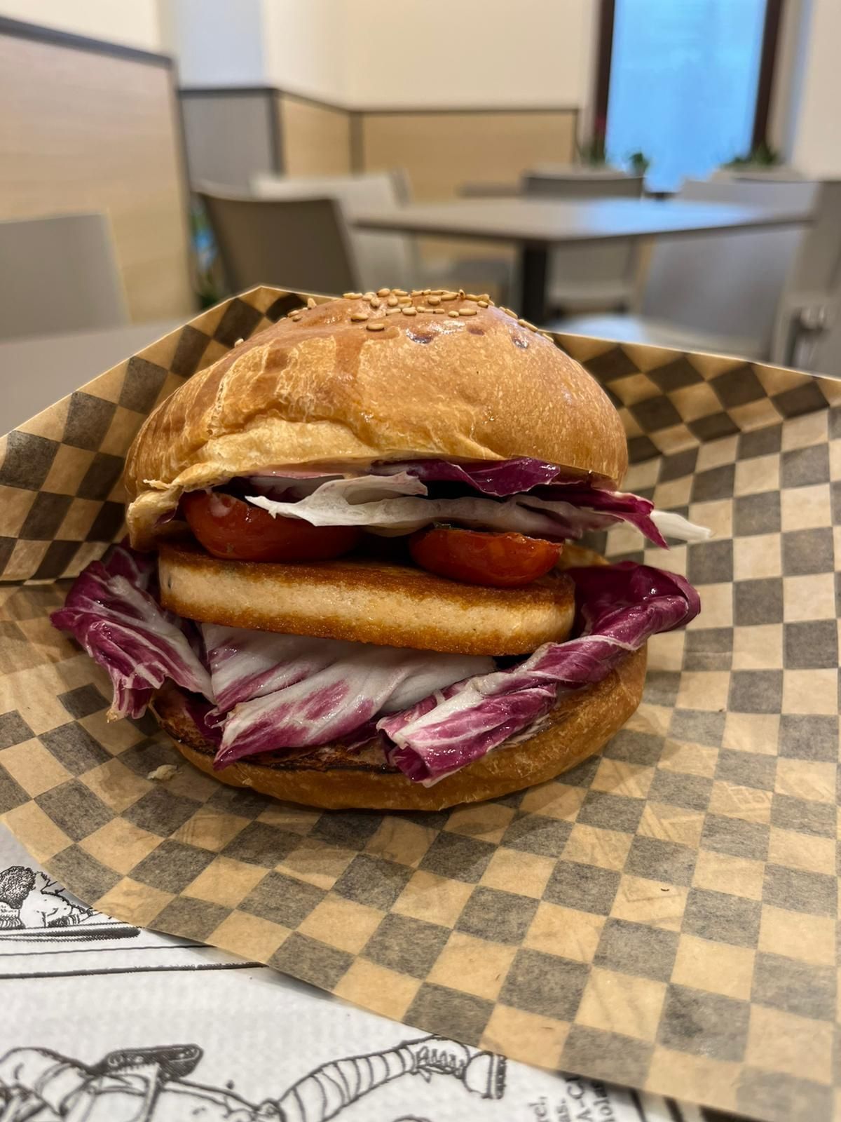 Panino con insalata di cavolo viola su carta a quadretti, servito su un tavolo da mensa.