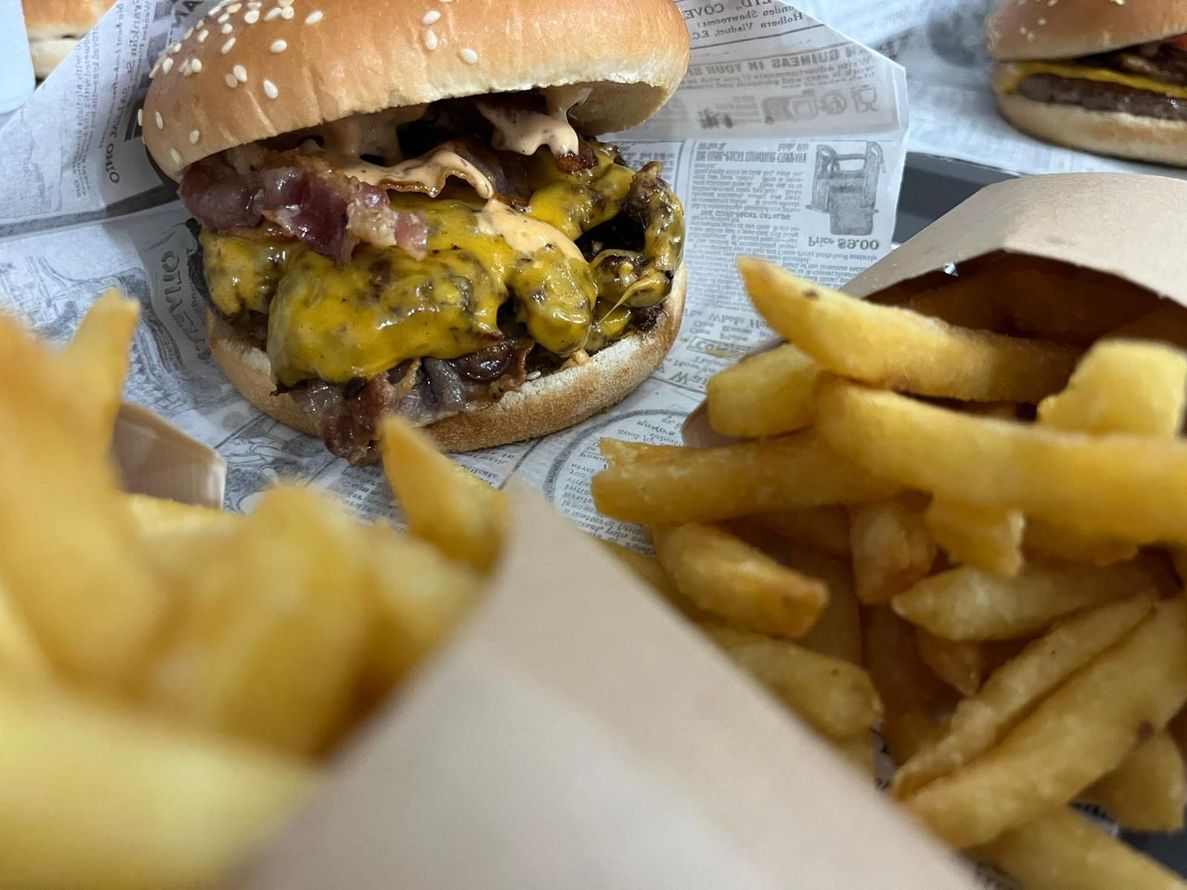 Cheeseburger con formaggio fuso e patatine fritte su un vassoio, avvolto nella carta