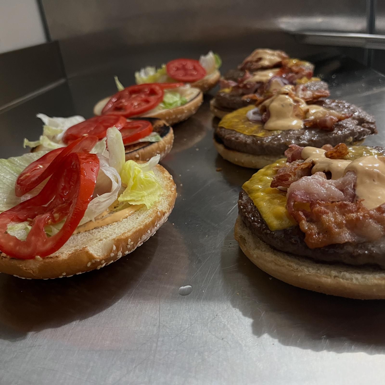 Vassoio di mini hamburger con lattuga, pomodoro, formaggio e pancetta su una superficie in acciaio inox.