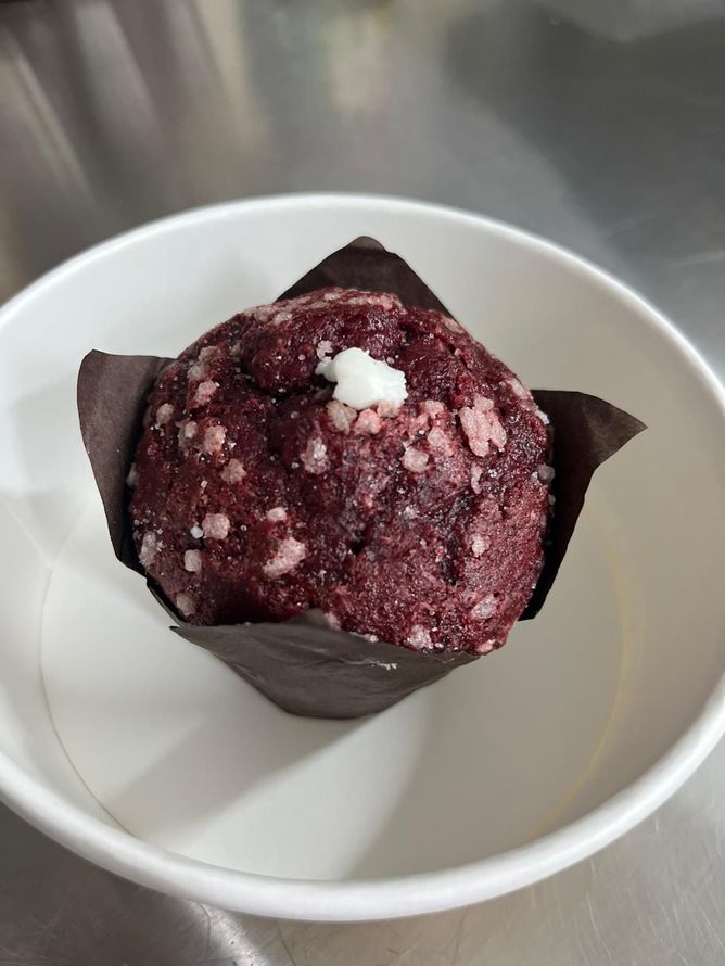 Muffin ai frutti di bosco scuri in un involucro marrone su una ciotola bianca in un supporto di acciaio inossidabile.