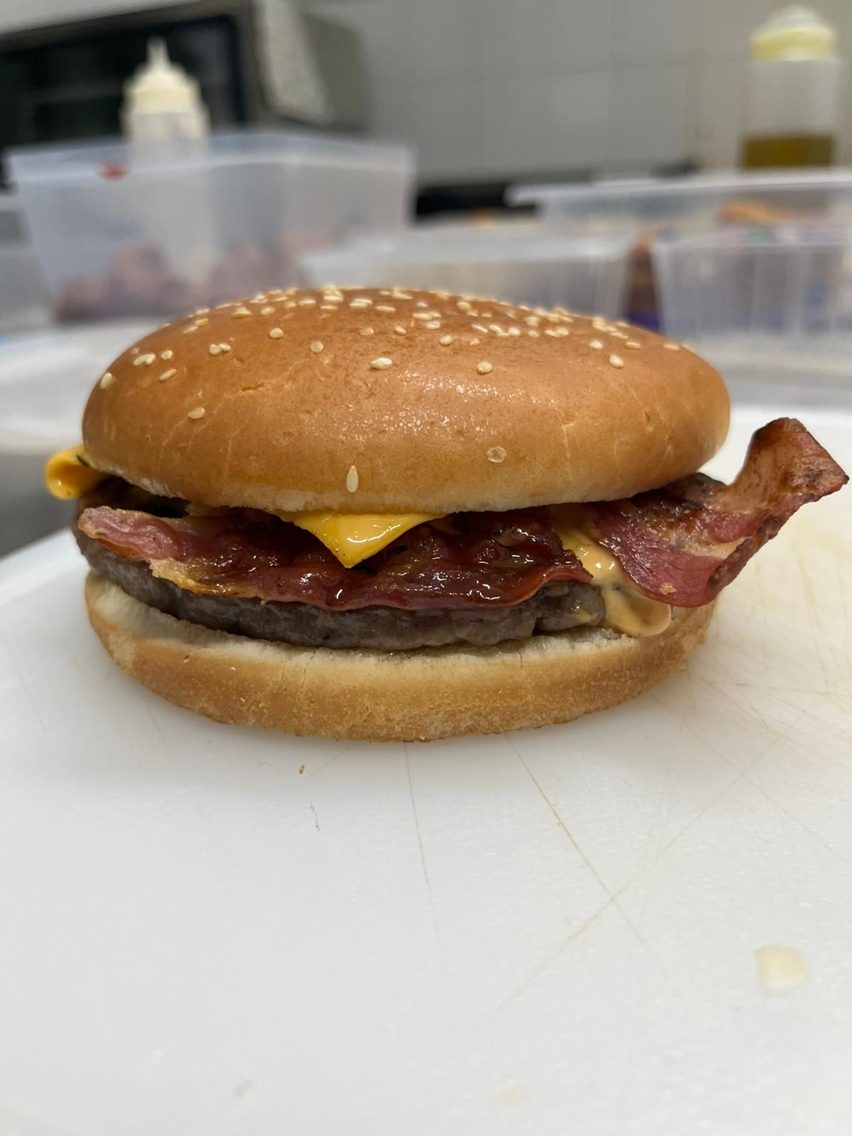 Cheeseburger con pancetta su un panino al sesamo su un bancone di lavoro, con formaggio fuso e una striscia di pancetta ben visibili.