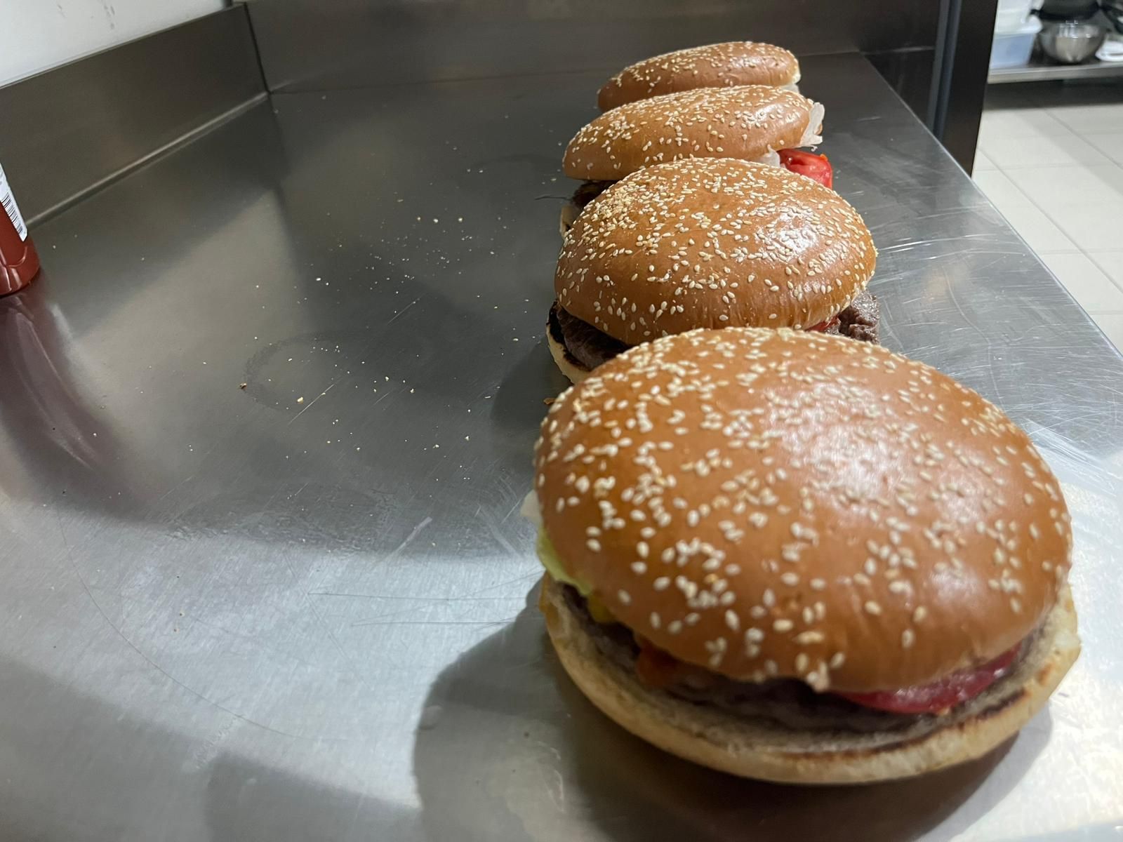 Tre hamburger con semi di sesamo allineati su un bancone di metallo in una cucina