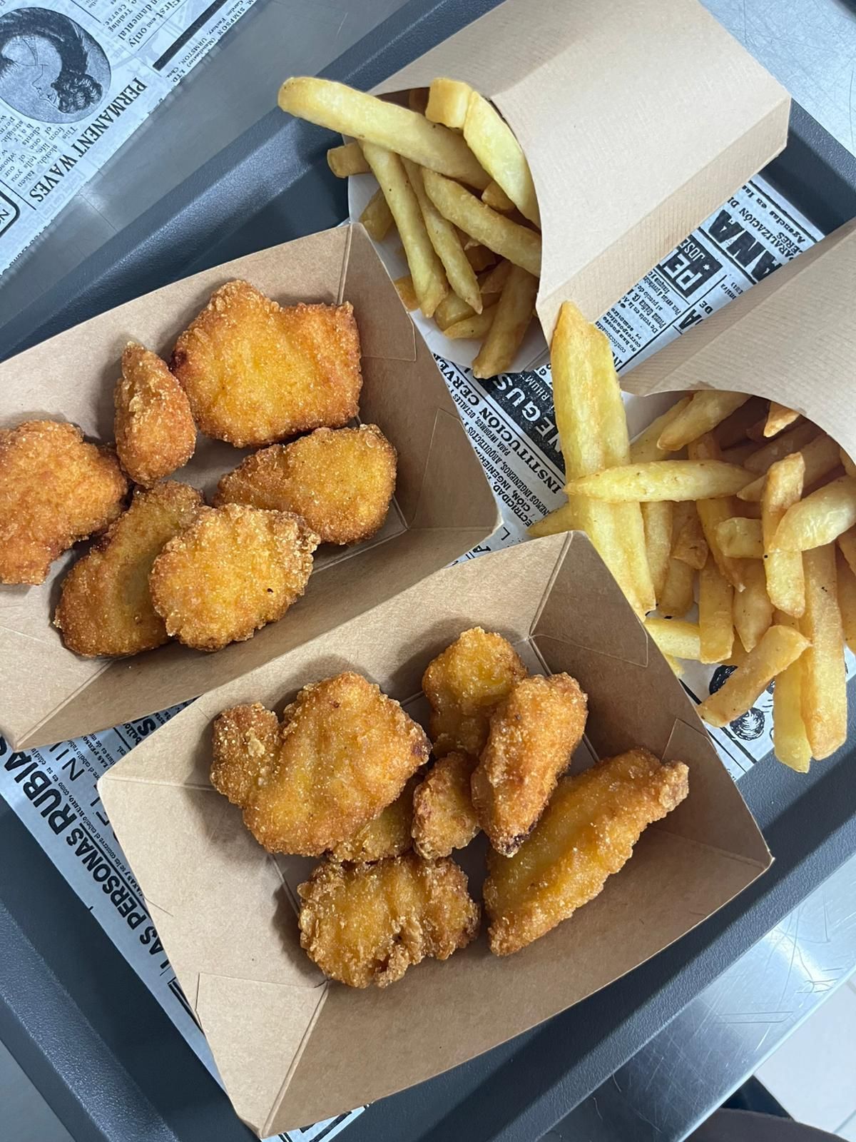 Due scatole di crocchette di pollo fritte e patatine fritte su un vassoio rivestito di carta di giornale.