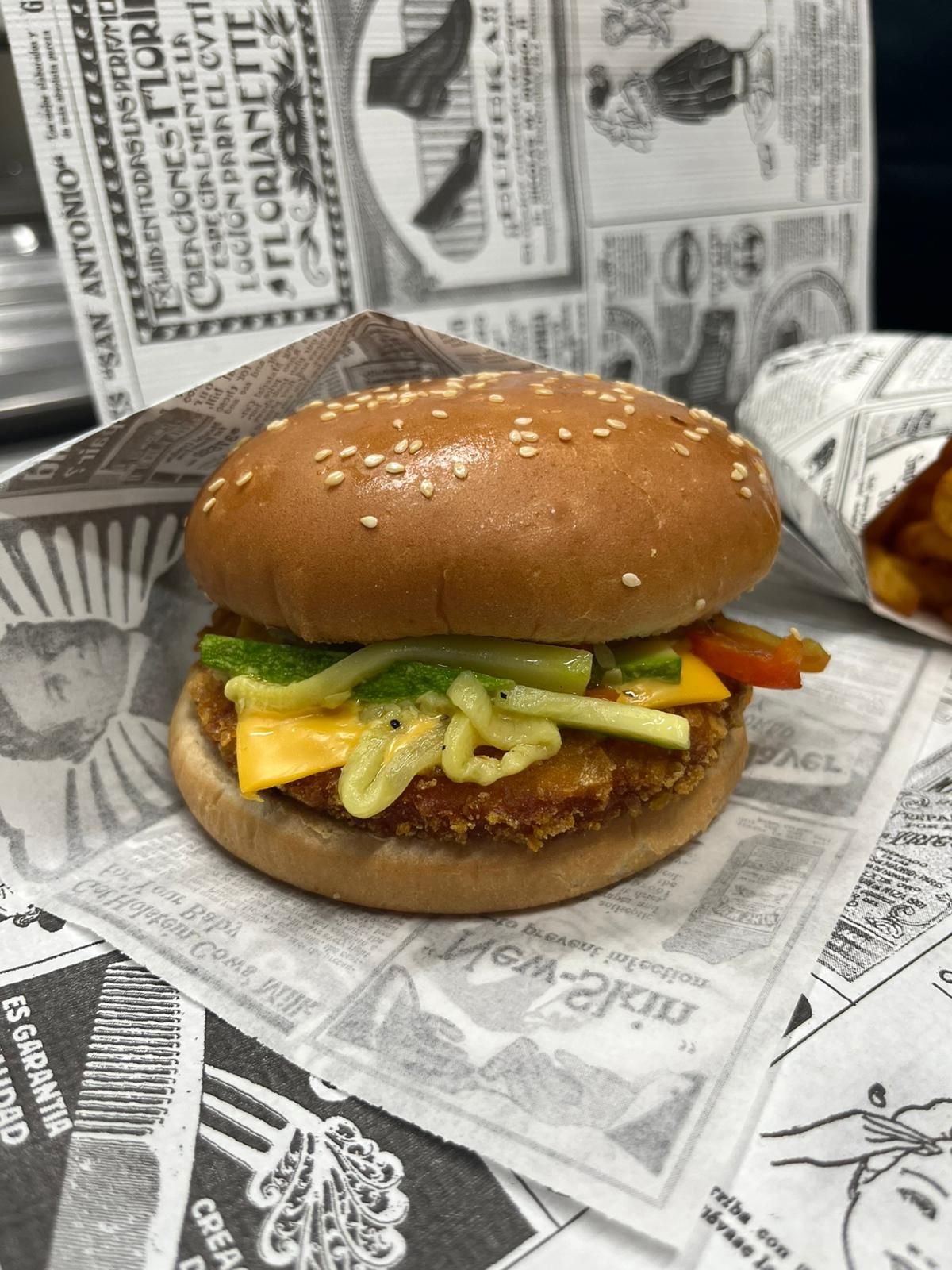 Hamburger al sesamo con lattuga, formaggio e patatine fritte su un vassoio foderato di giornale, con il sacchetto delle patatine sullo sfondo.