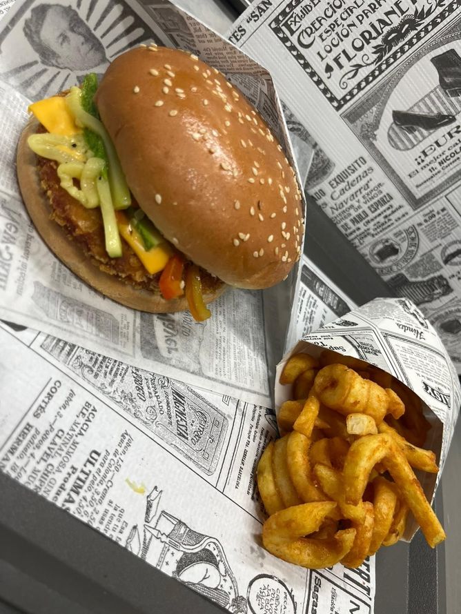 Hamburger e patatine fritte ricce su carta tipo giornale, con lattuga e pomodoro visibili.