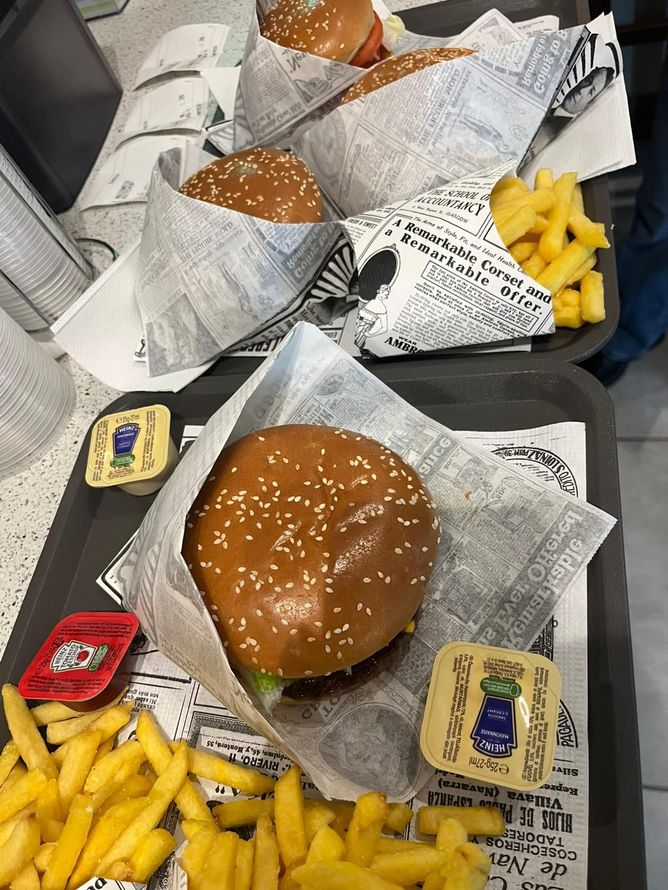 Vassoi di fast food con hamburger, patatine fritte e bustine di condimenti su un tavolo.
