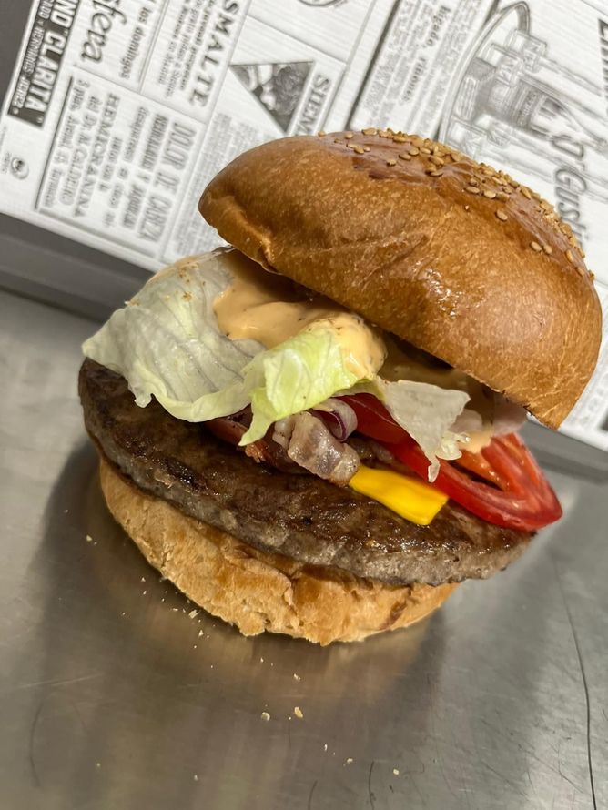 Hamburger di manzo con lattuga, formaggio e pomodoro in un panino, servito su una superficie metallica.