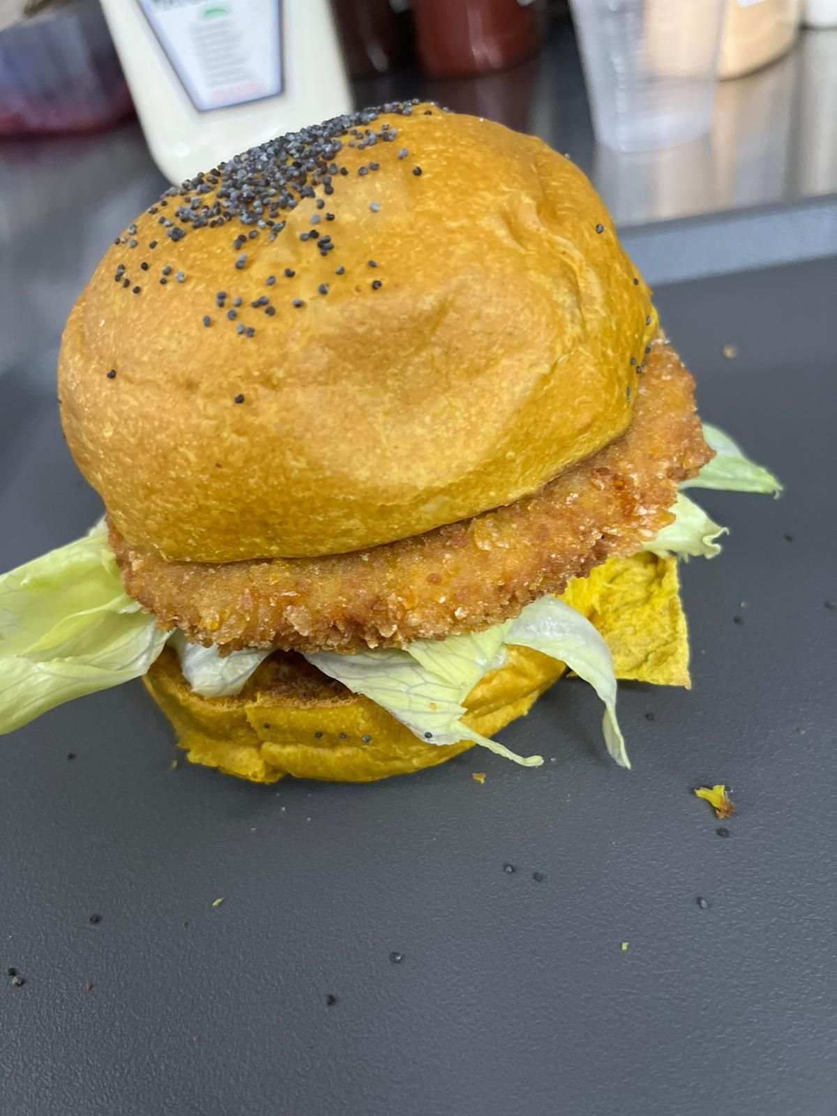 Panino al sesamo con lattuga e salsa su un vassoio scuro con briciole