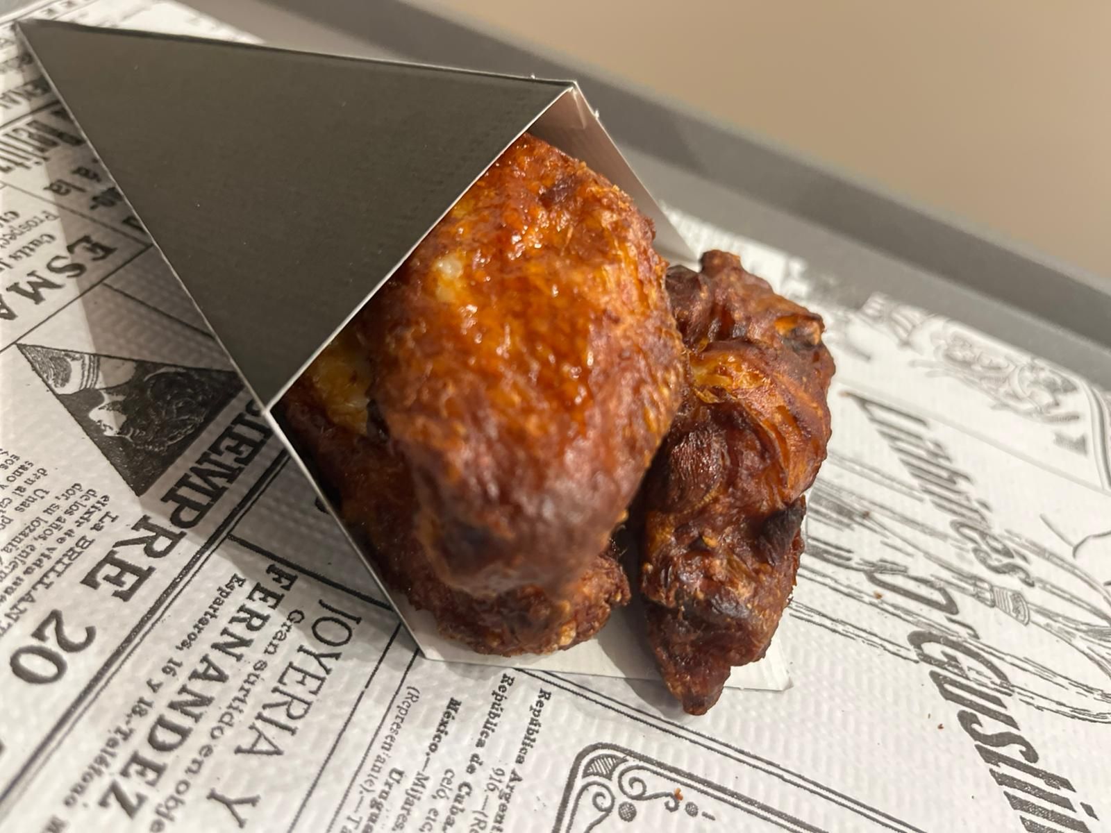 Due ali di pollo glassate in un cono di metallo su carta foderata di giornale