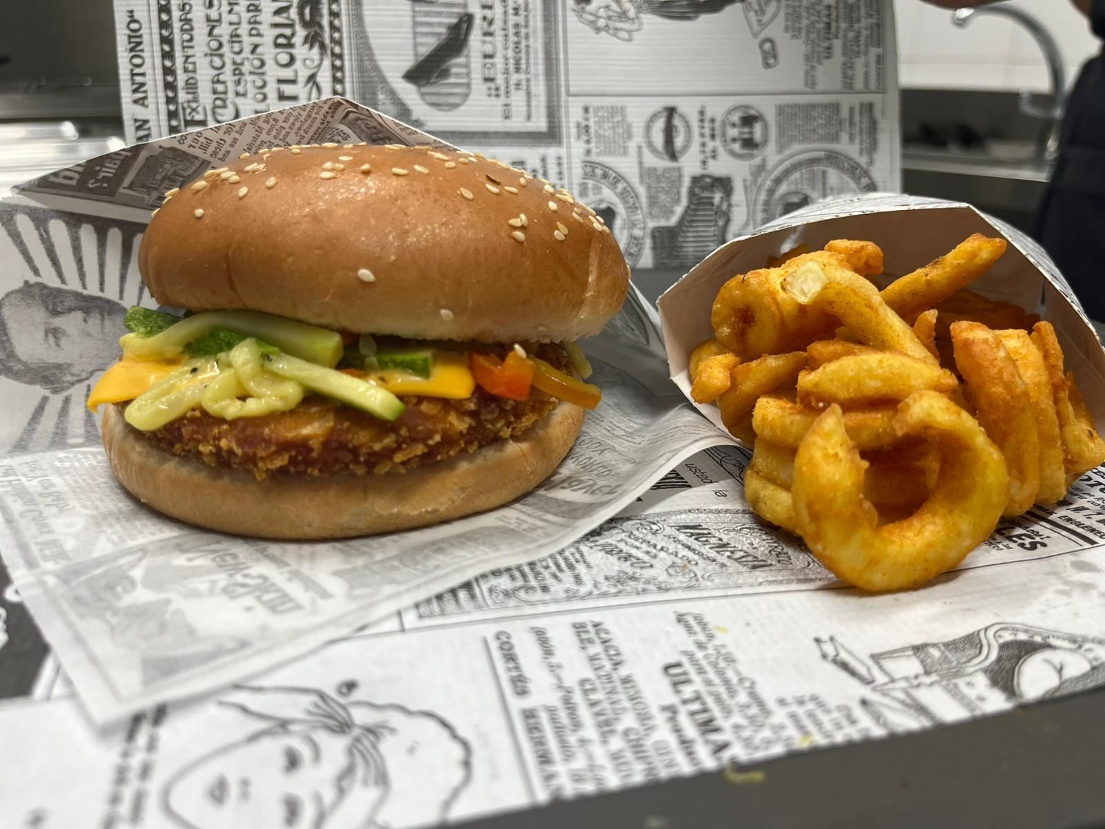 Hamburger e patatine fritte ricce serviti in cestini foderati di carta su un tavolo allestito come un giornale.