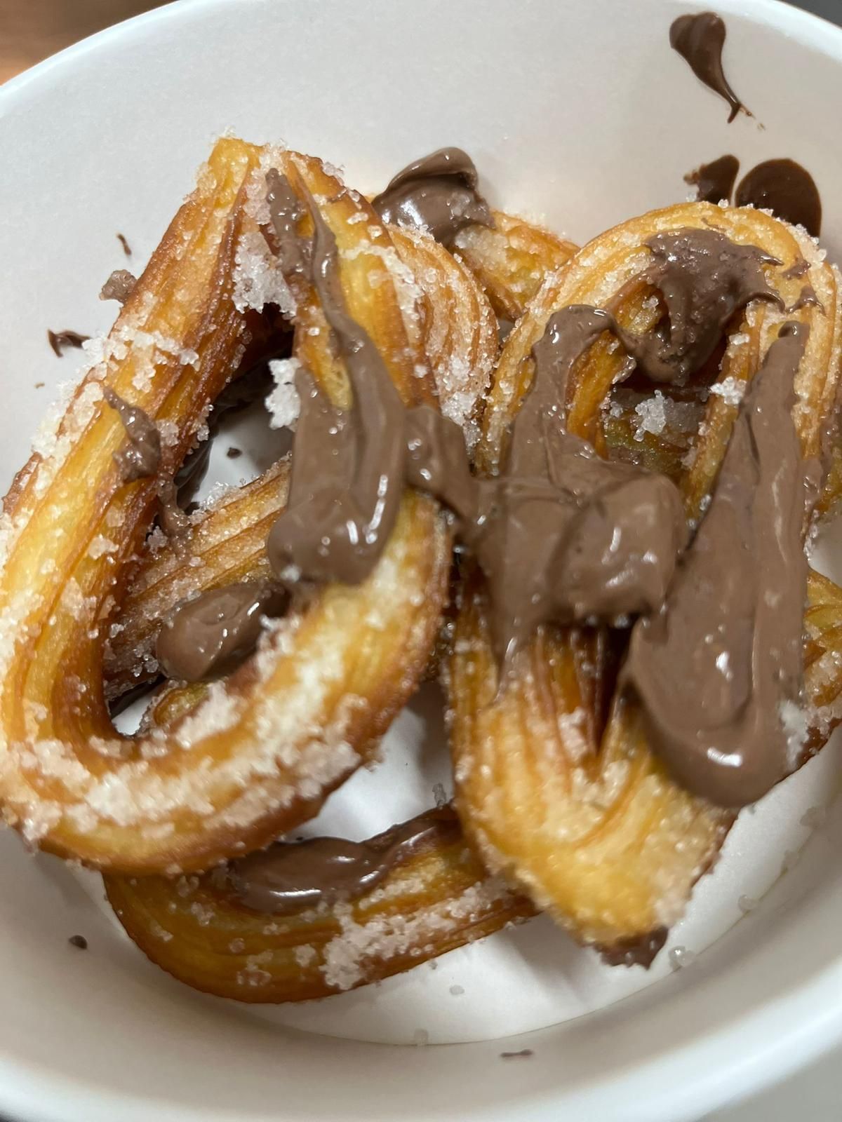 Churros in una ciotola bianca ricoperti di salsa al cioccolato fuso