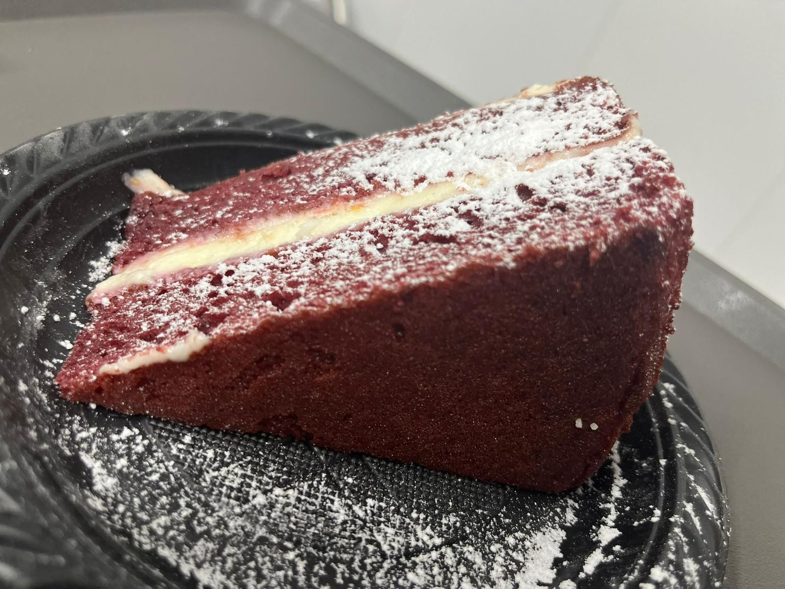 Fetta di torta red velvet spolverata di zucchero a velo su un piatto nero