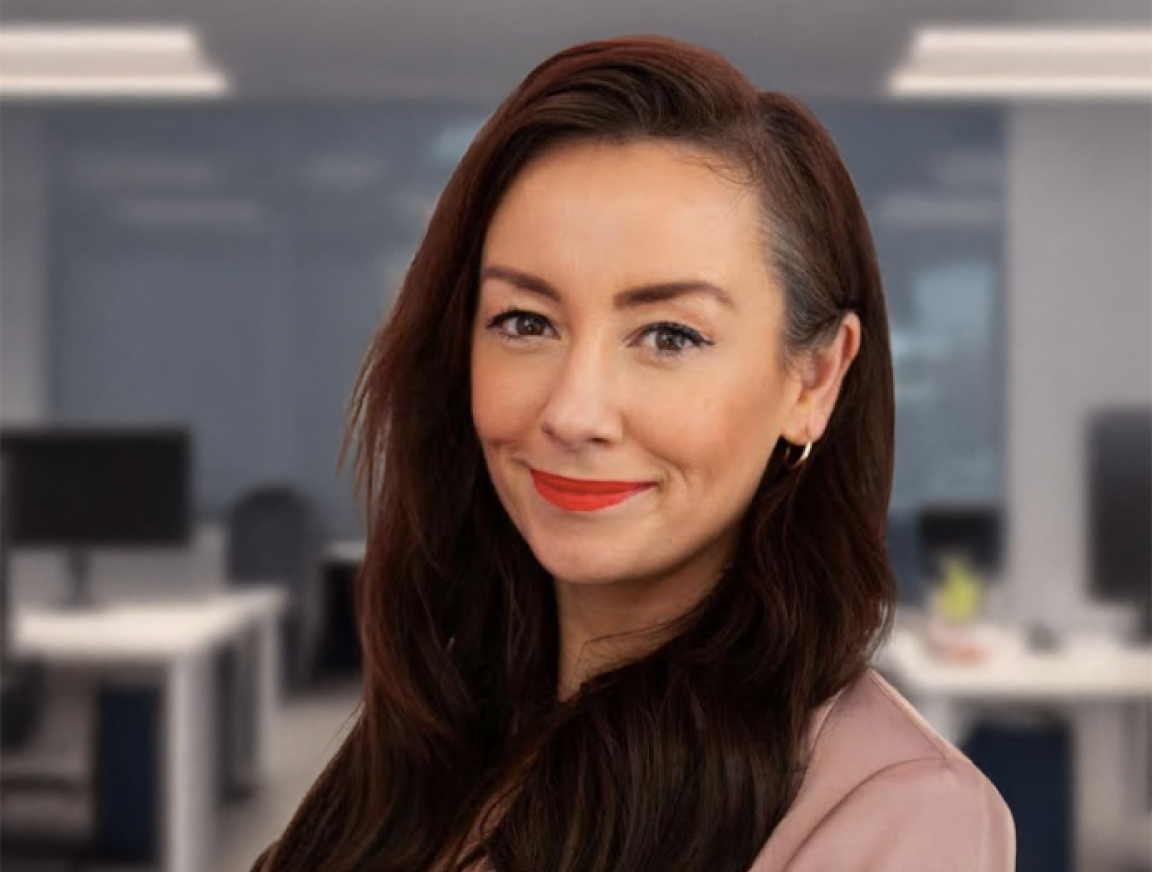 A woman with long brown hair and red lips is smiling in an office.