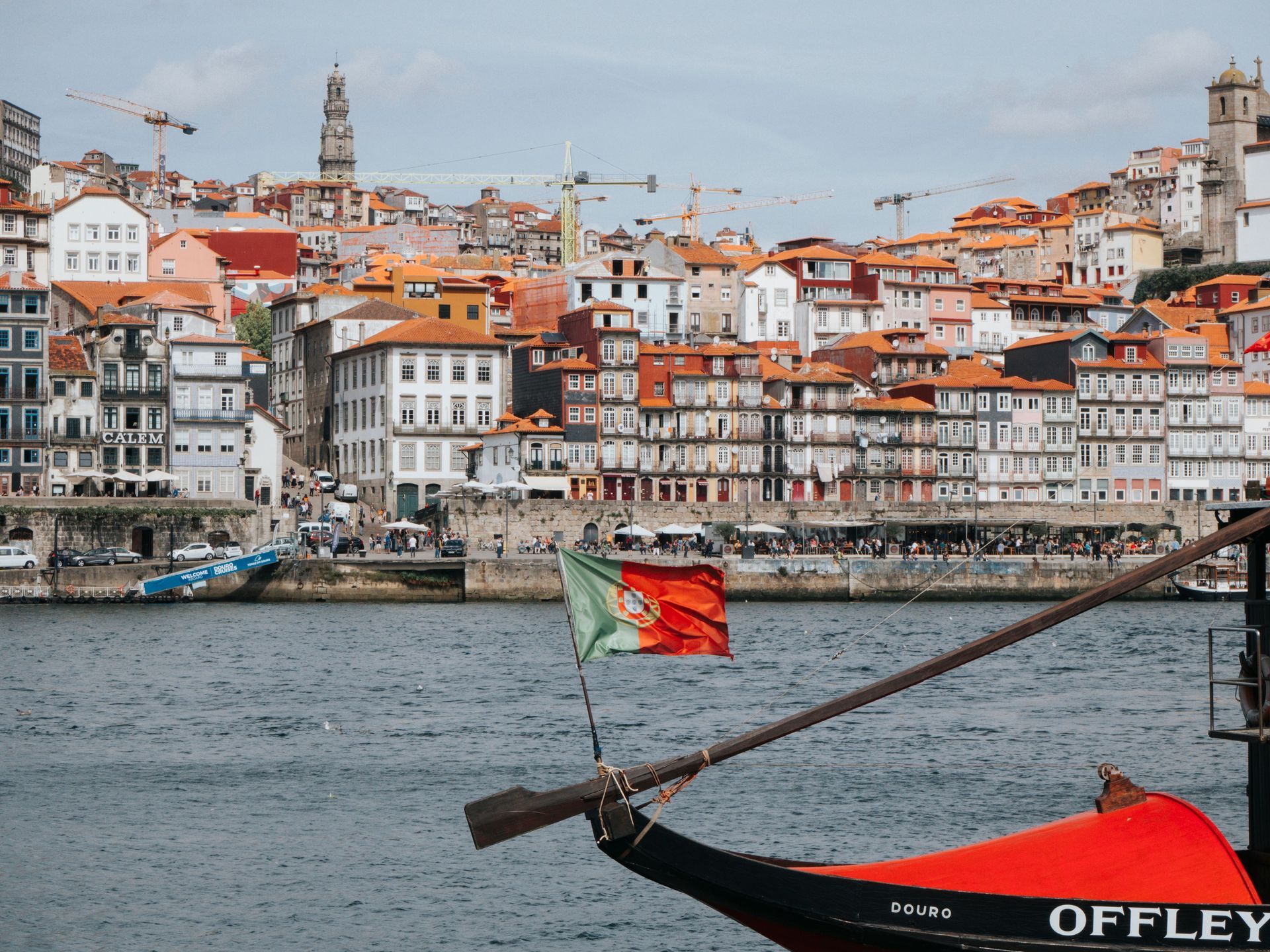 Boat with Portuguese flag on a river in front of a hillside city of red-roofed buildings