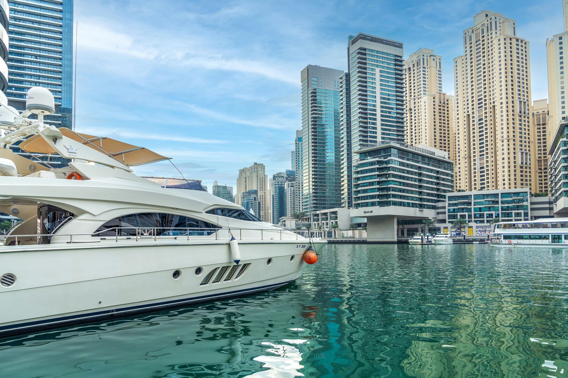 A white yacht is docked in a harbor with a city skyline in the background.