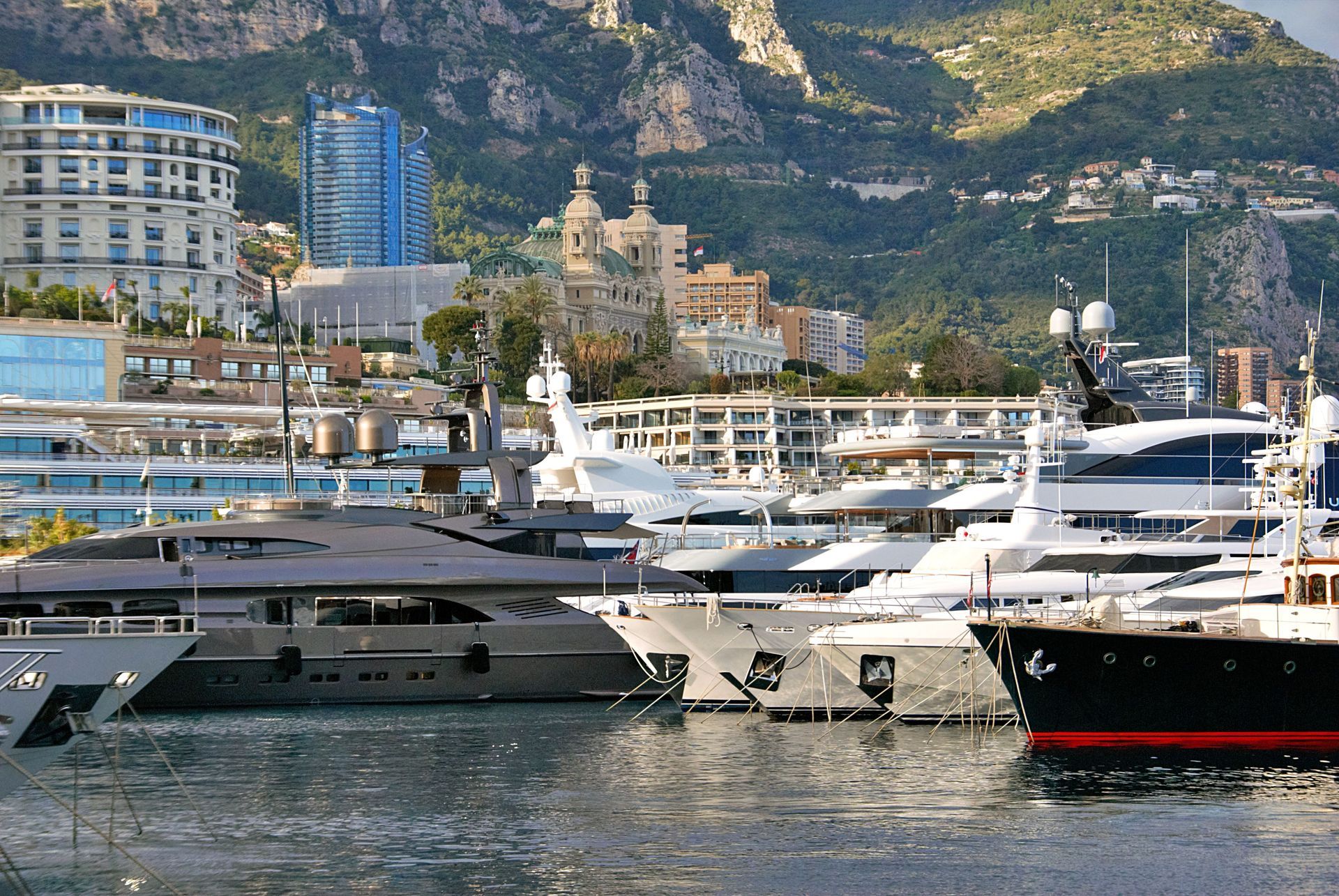 Luxury yachts docked in a harbor with a mountain town and buildings in the background