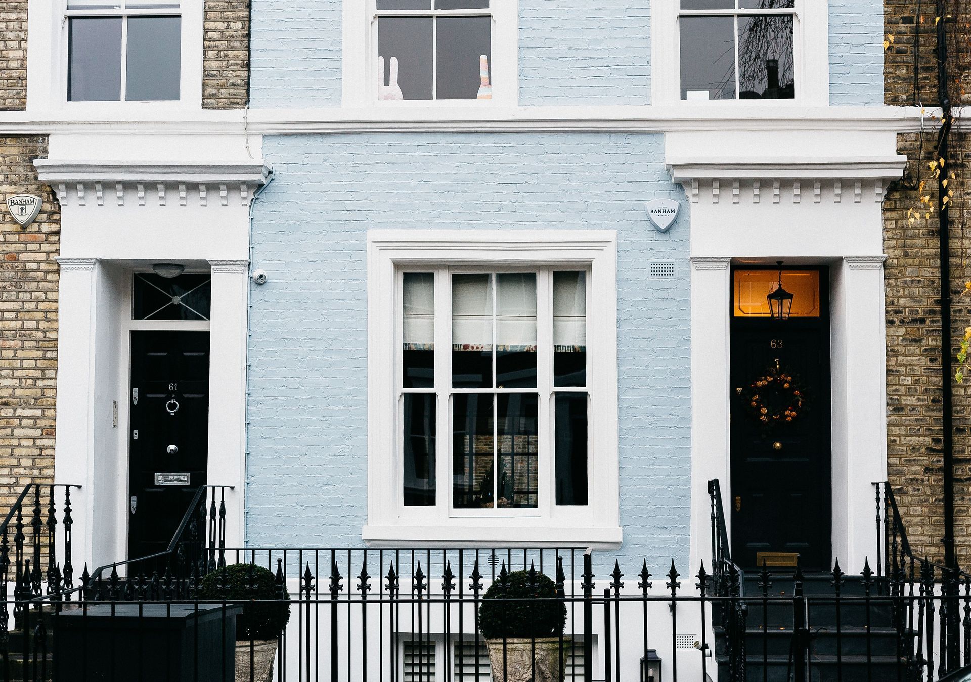 Row of London pastel townhouse facades with black doors, white trim, and wrought-iron railings