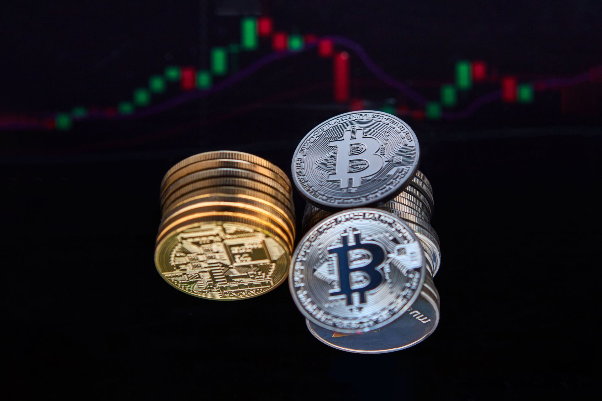 Bitcoin and gold coins in front of a blurred red-and-green trading chart