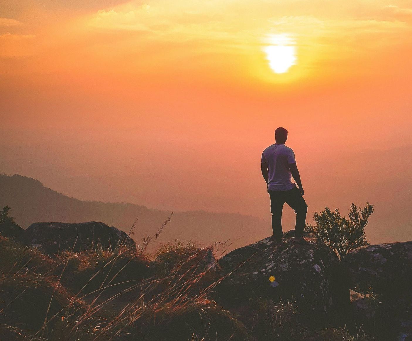 A man is standing on top of a hill looking at the sunset.