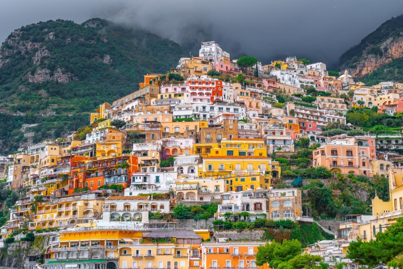 Colorful hillside town with stacked buildings nestled among green mountains under cloudy skies