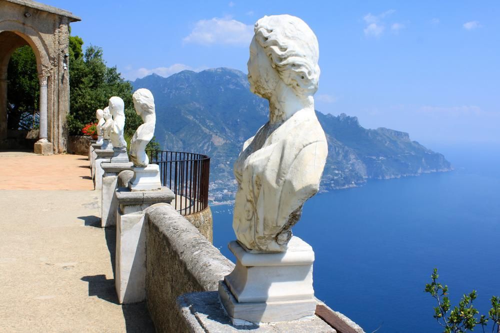 Marble busts along a seaside terrace overlooking blue water and distant mountains