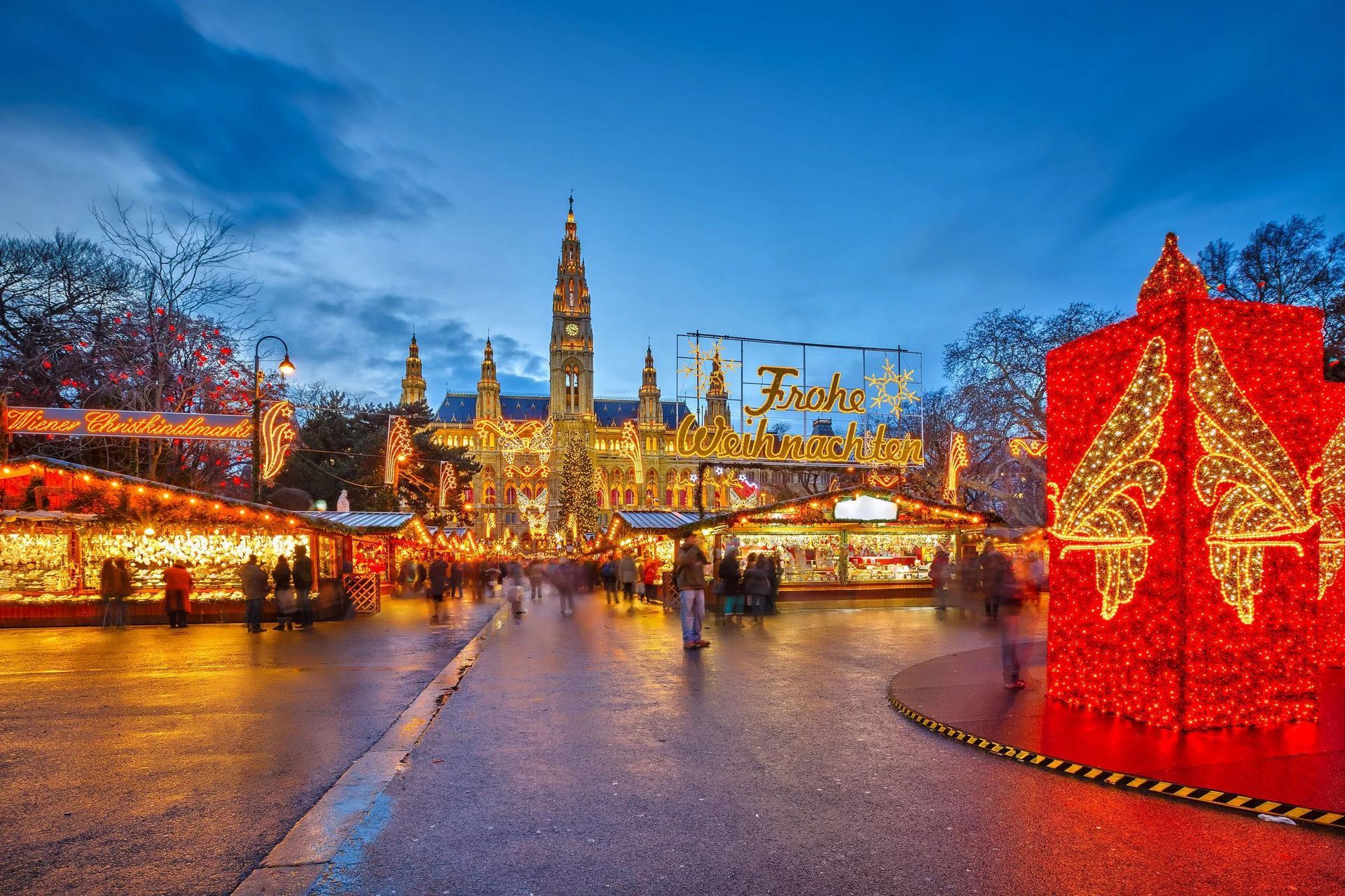 Festive winter market at dusk with glowing lights, a tall tower, and a red illuminated star display