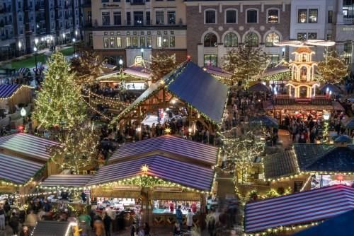 Busy holiday market at night with illuminated stalls, decorated trees, and a large crowd