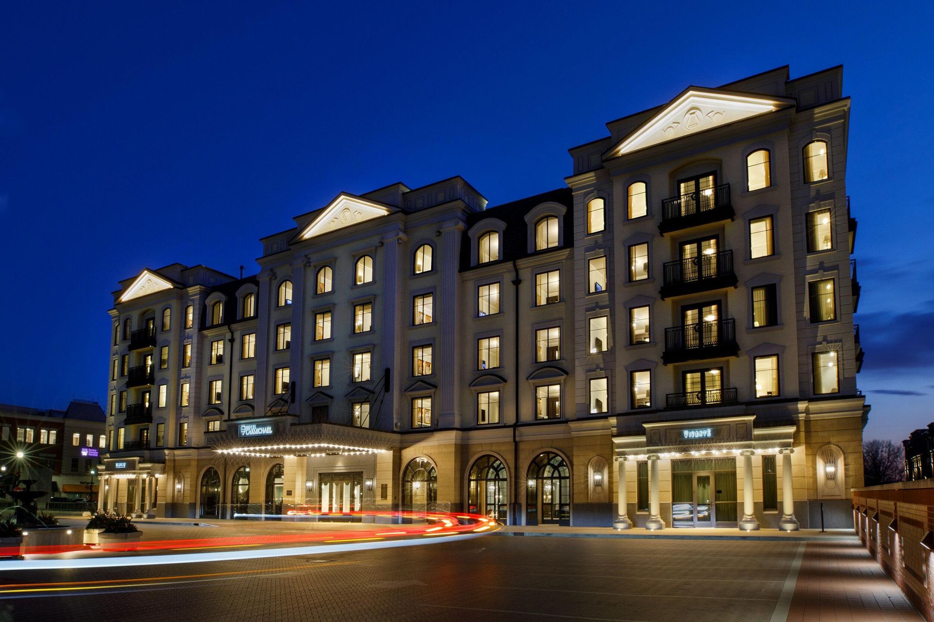 Illuminated multi-story hotel at night with cars passing in front and a deep blue sky