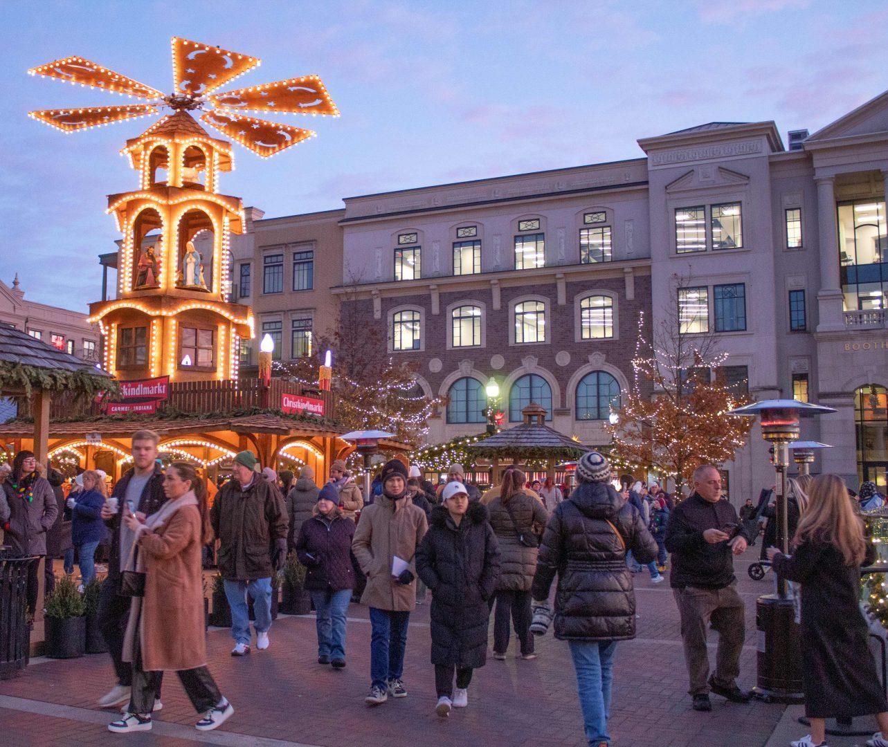 Crowded holiday market at dusk with a lit windmill and festive stalls in a city square